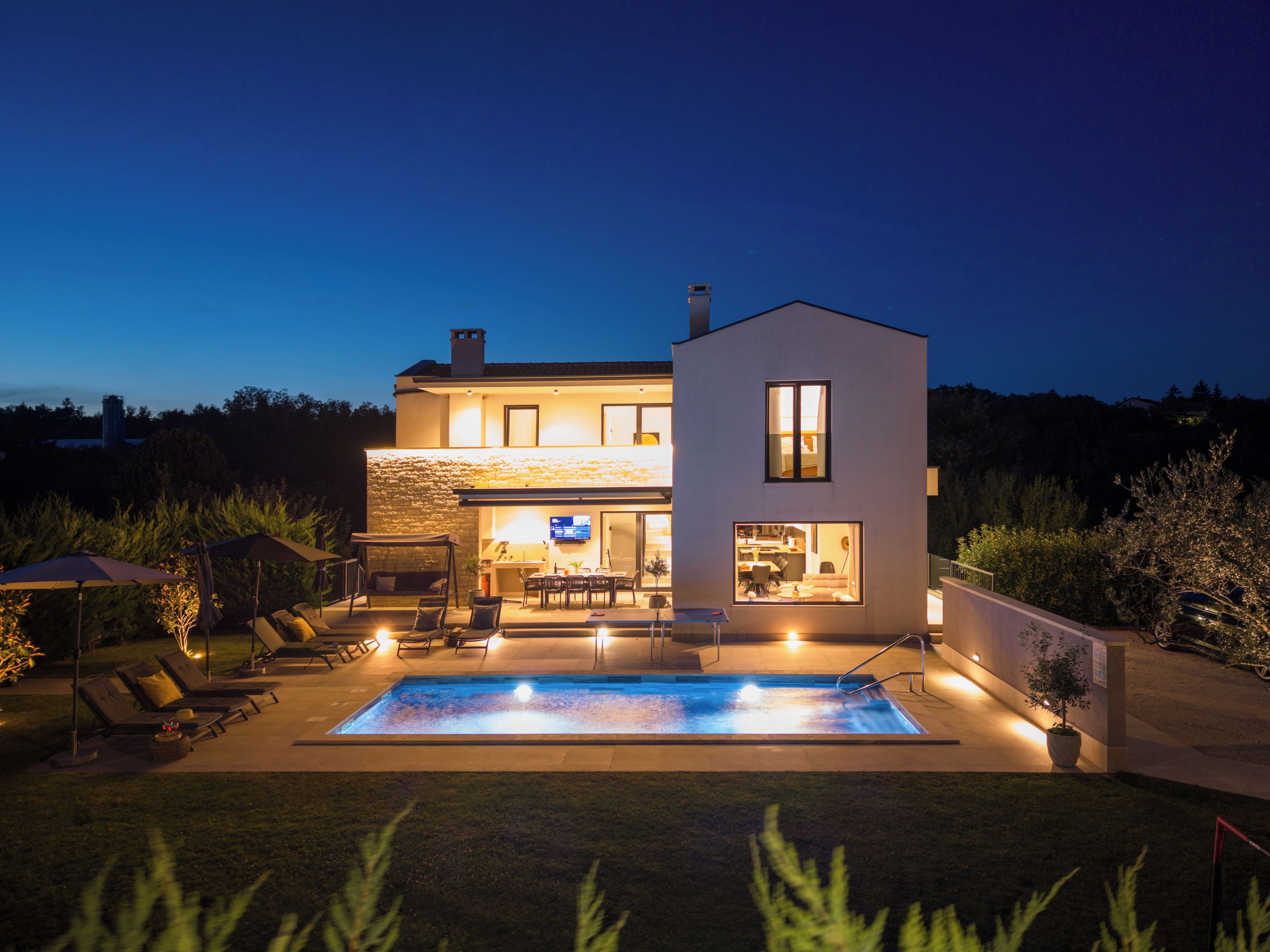 Une maison moderne dotée d’une piscine, d’un espace salon extérieur et d’un patio bien éclairé.