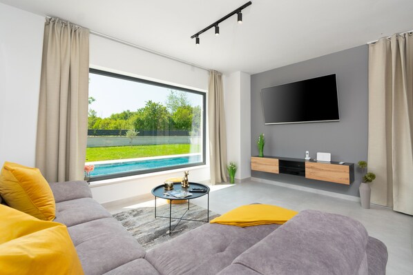 A modern living room with a large window, a flat-screen TV, and a minimalist design. - Modern 300m² Villa • King Beds & Leisure Zone (Kringa)