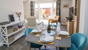 Un coin repas avec une table dressée pour quatre personnes, des chaises, un téléviseur et une vue sur l’extérieur.