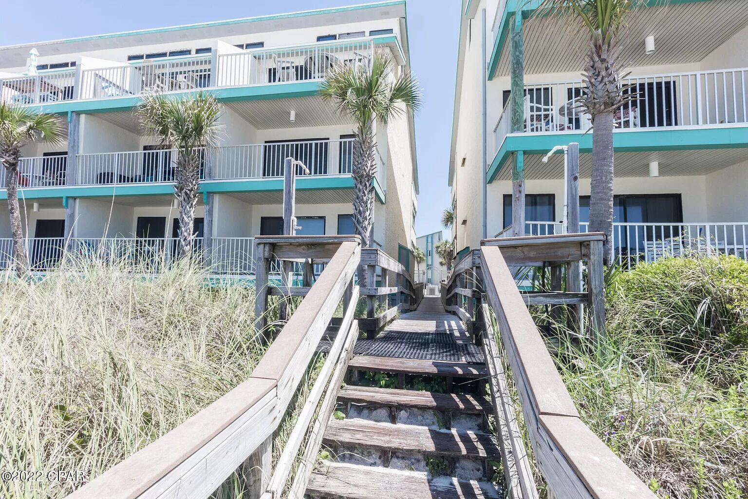 A wooden staircase leading to a building with multiple balconies and a beachside view.