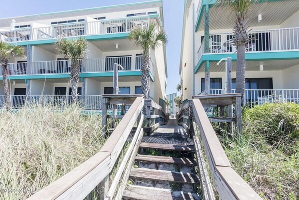 A wooden staircase leading to a building with multiple balconies and a beachside view.