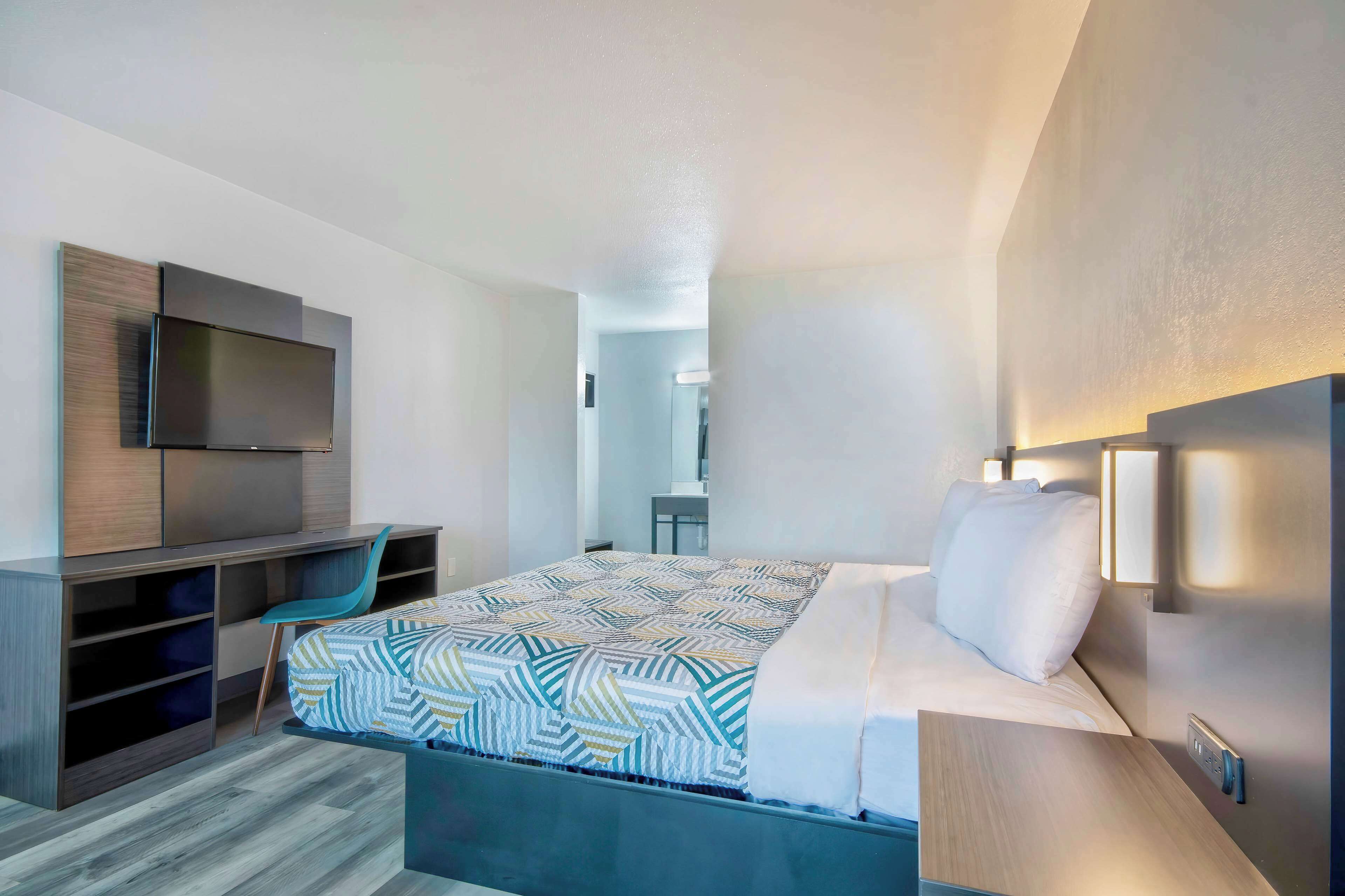 A modern hotel room with a bed, a desk, and a TV.