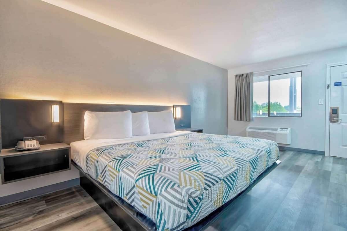 A hotel room with a bed, bedside table, and a window.