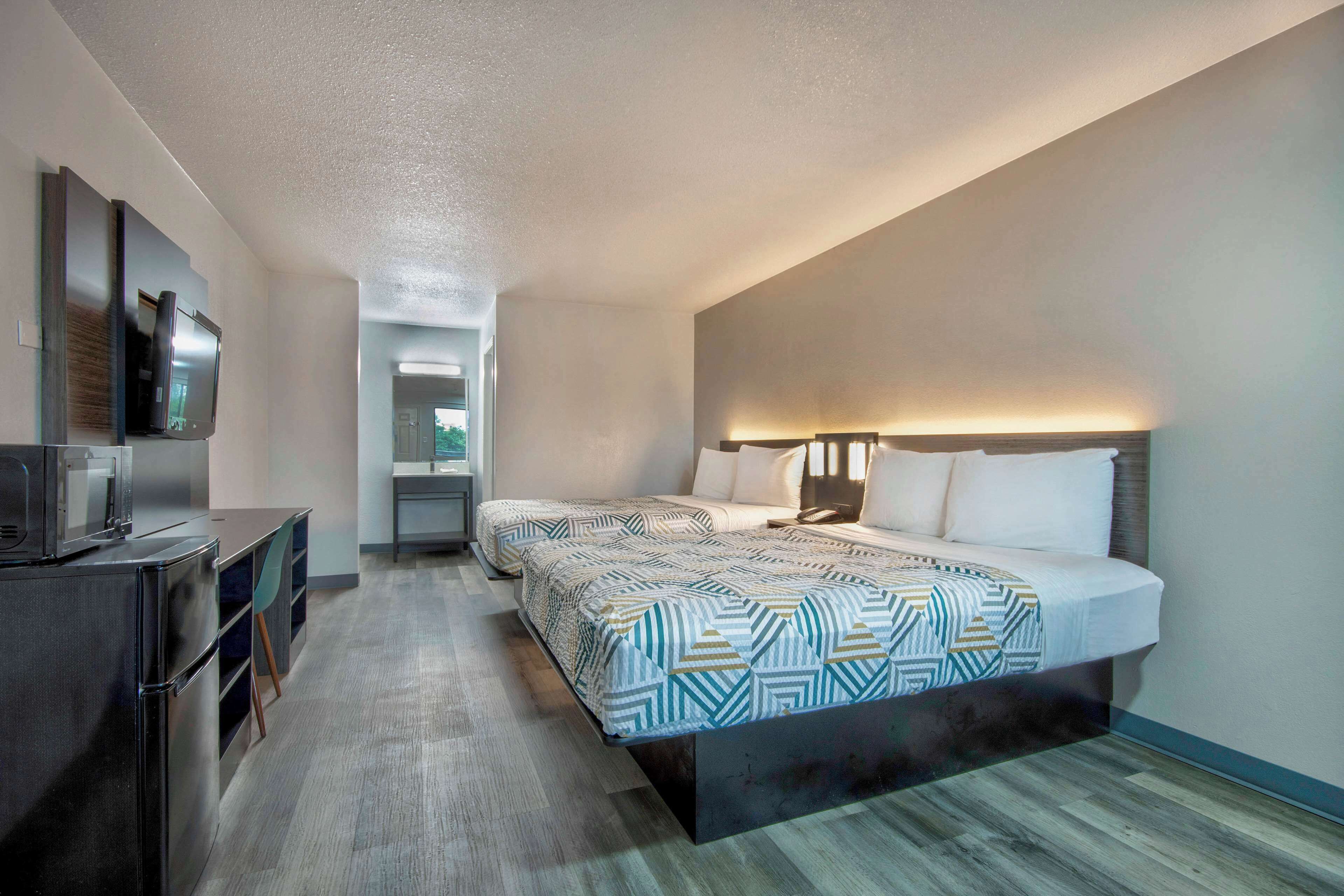 A hotel room with a bed, bedside table, TV, and a desk with a chair.