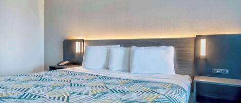 A hotel room with a bed, a nightstand, and a wall-mounted lamp.