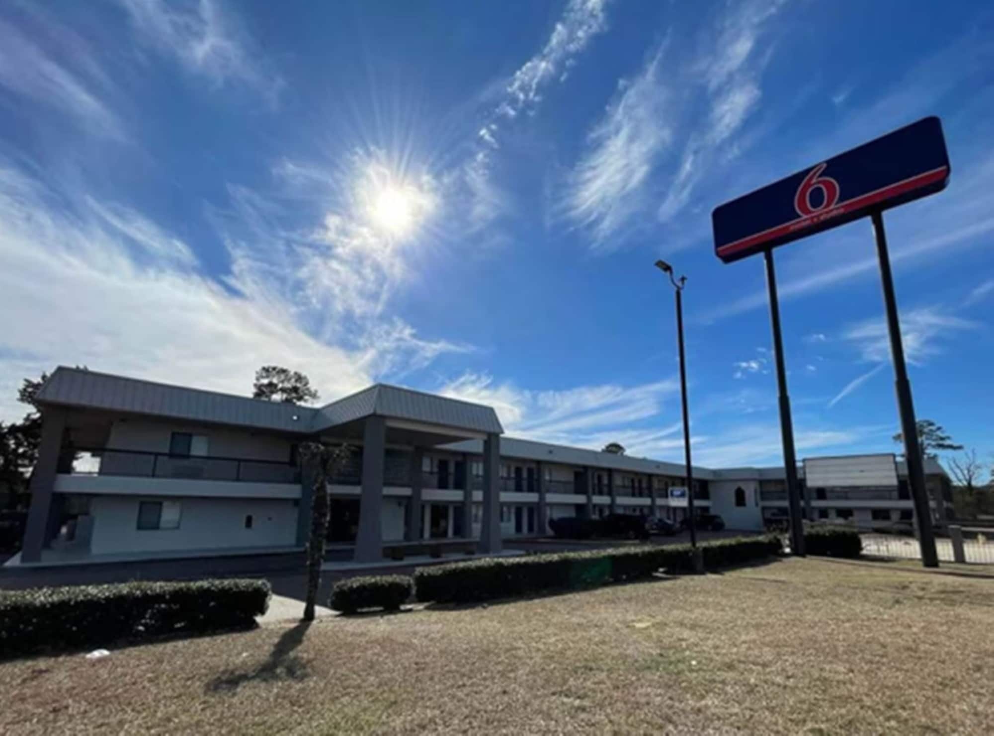 Un motel avec une grande enseigne sur laquelle est affiché le chiffre 6, un bâtiment moderne doté d’un toit plat et un parking.