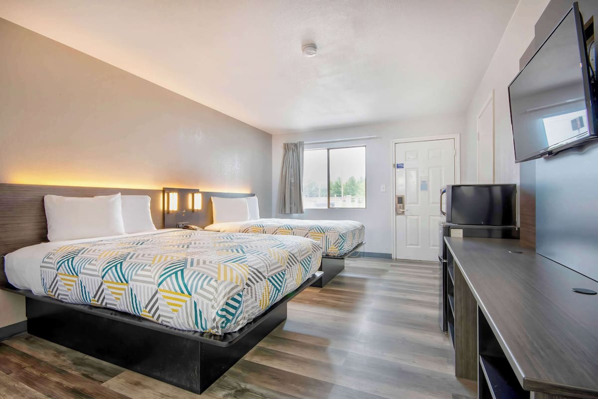 A hotel room with two beds, a TV, and a desk.