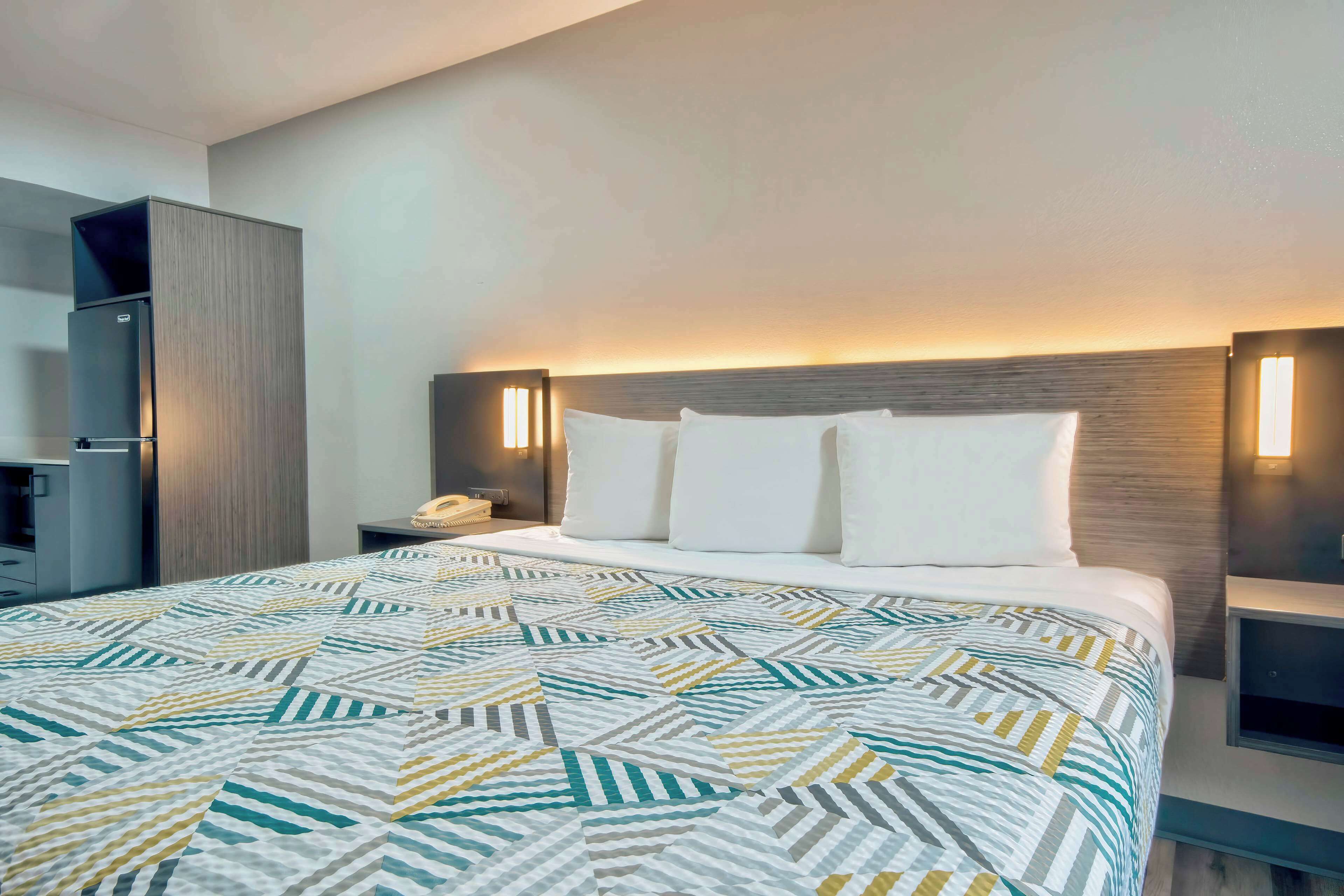 Una habitación de hotel con una cama grande, una mesita de noche, un escritorio y un armario.