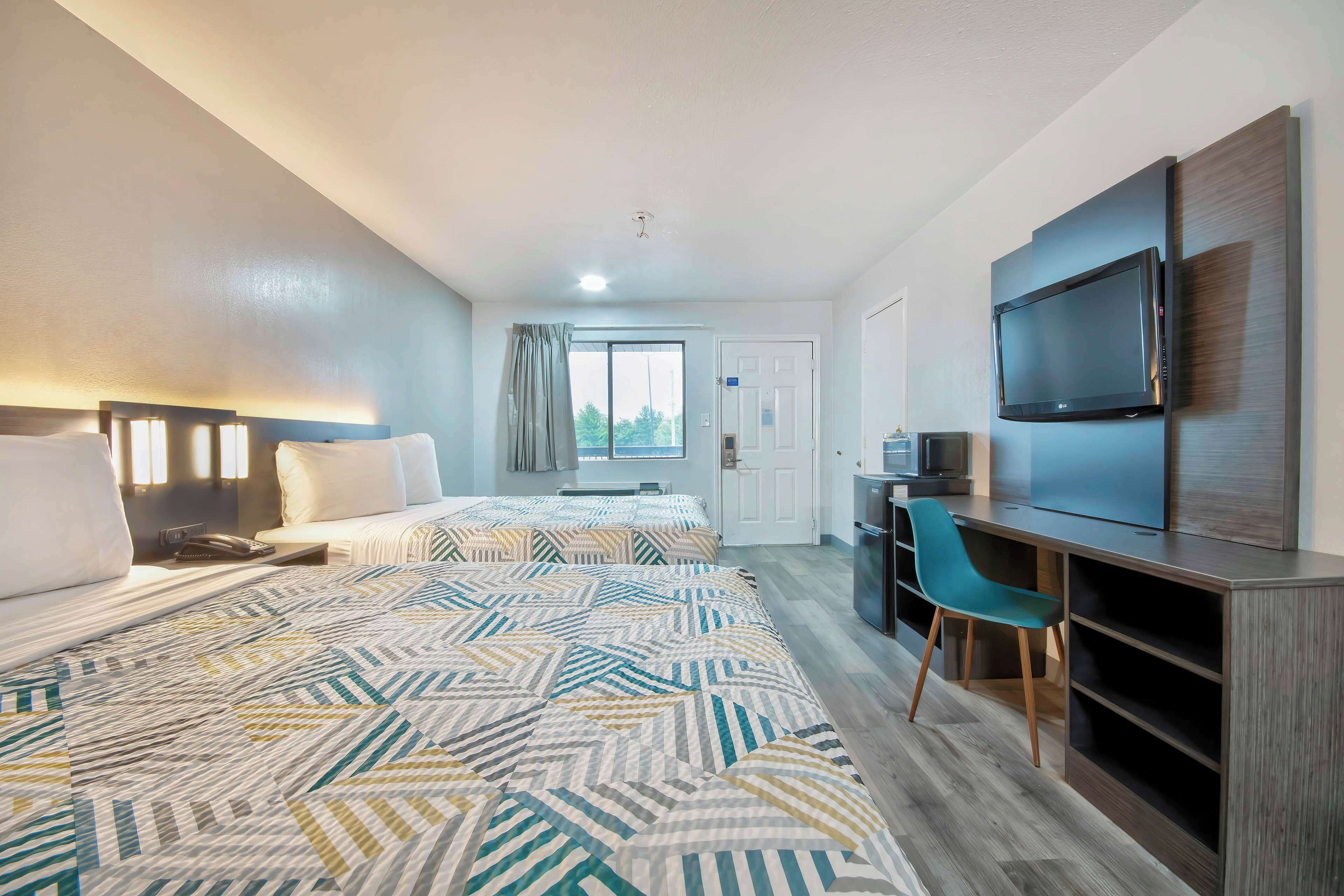 A hotel room with two beds, a desk, a television, and a chair.