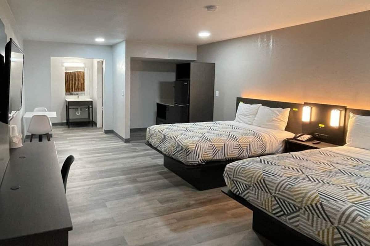 A hotel room with two beds, a desk, a television, and a bathroom visible in the background.