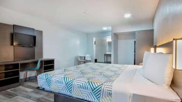 A modern hotel room with a large bed, a desk, a TV, and a bathroom visible in the background.