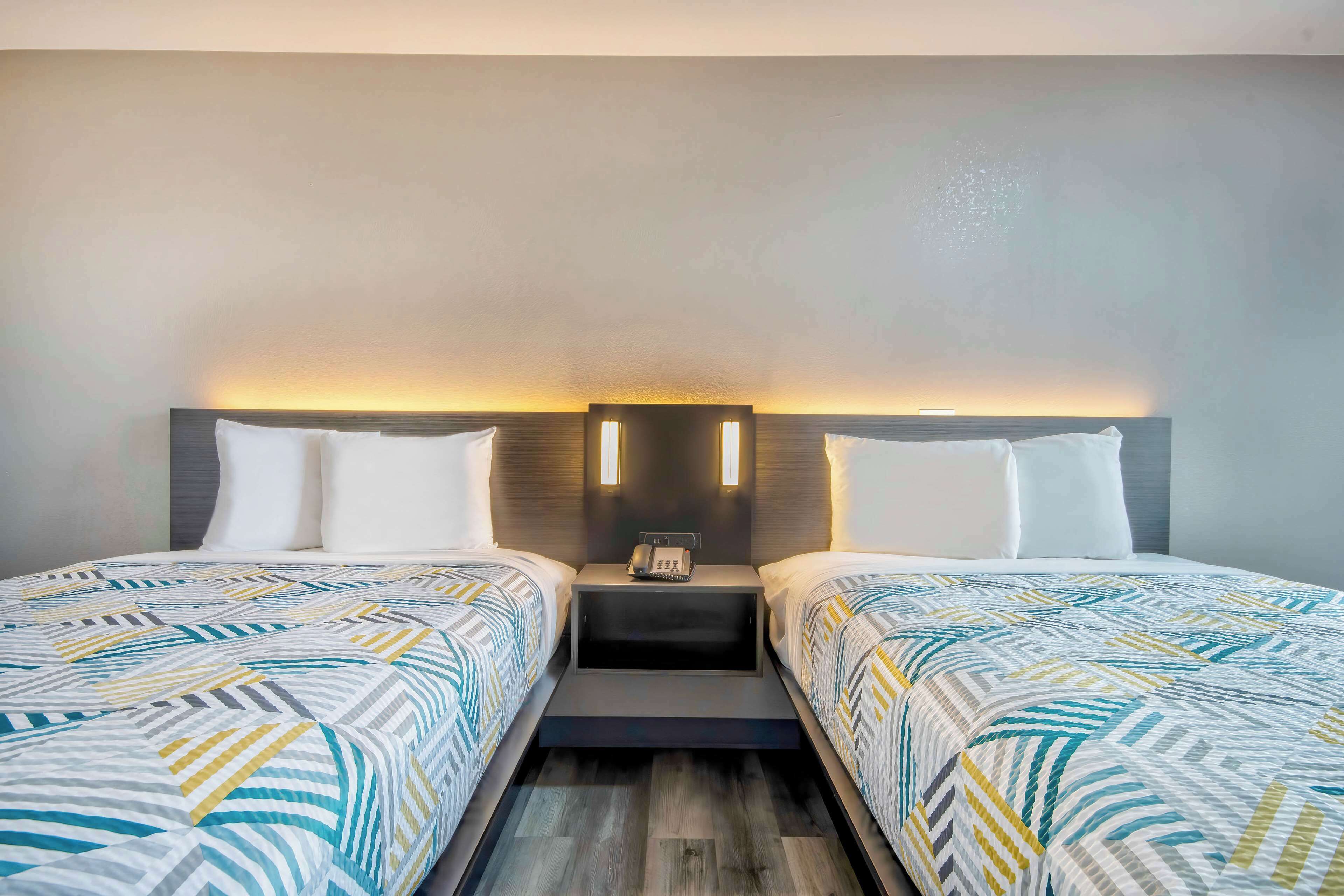 Een hotelkamer met twee bedden, een nachtkastje met een telefoon en een wandlamp.