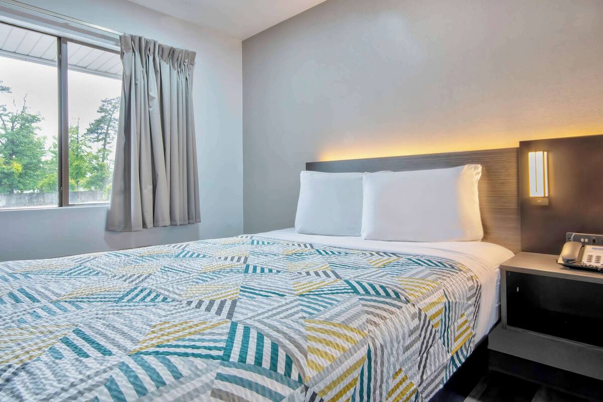 A hotel room with a large bed, a bedside table with a phone, and a window with curtains.