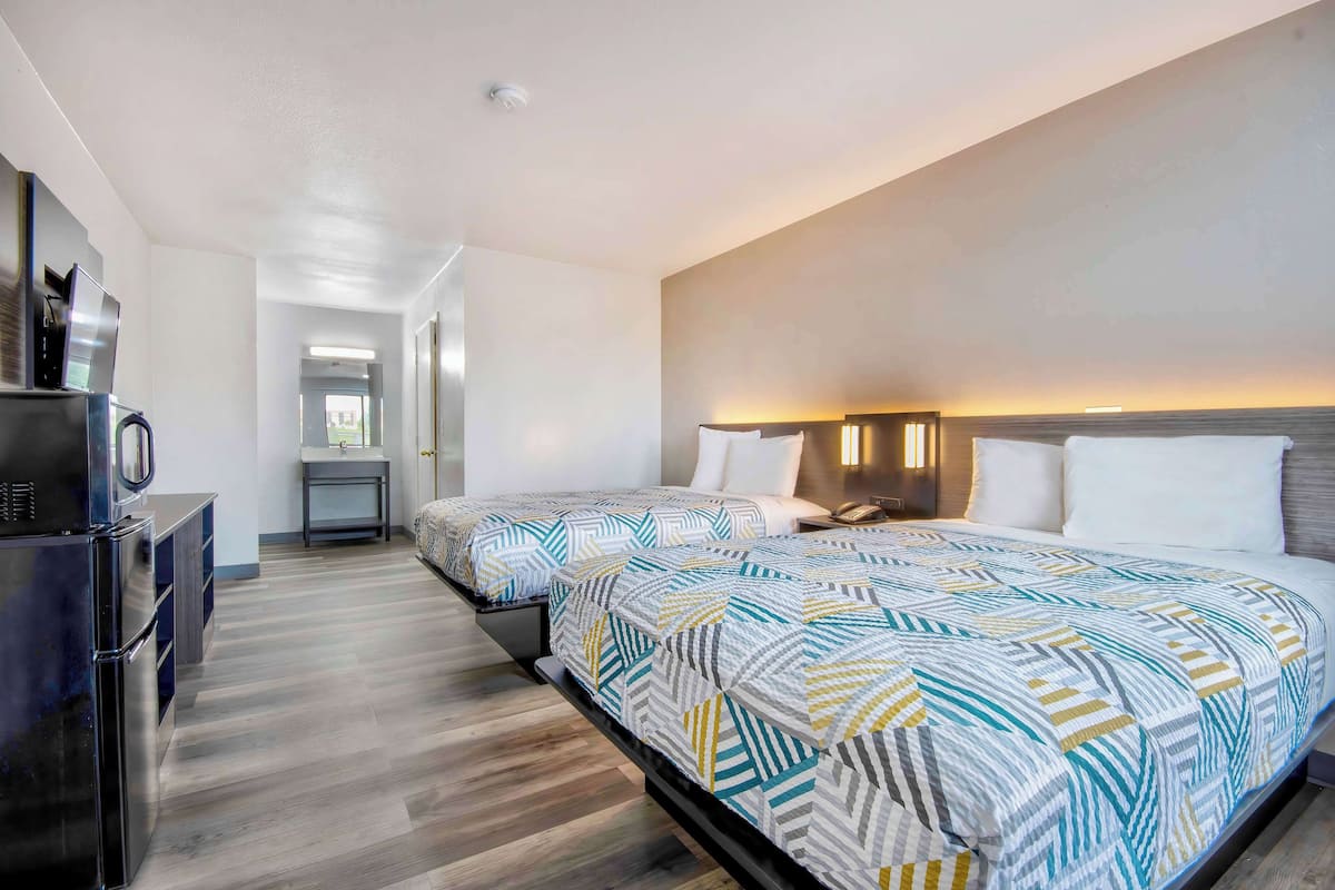 A hotel room with two beds, a kitchenette, and a bathroom.