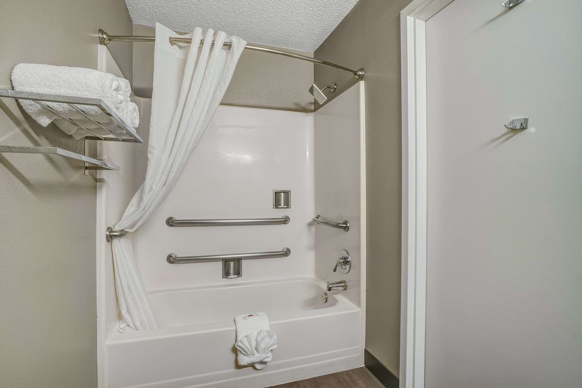 A modern bathroom with a walk-in shower, grab bars, a towel rack, and a shower curtain.