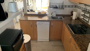 Kompakti keittiö, jossa on astianpesukone, liesi ja pesuallas. Keittiössä on myös pieni ruokailutila, jossa on pöytä ja tuolit.