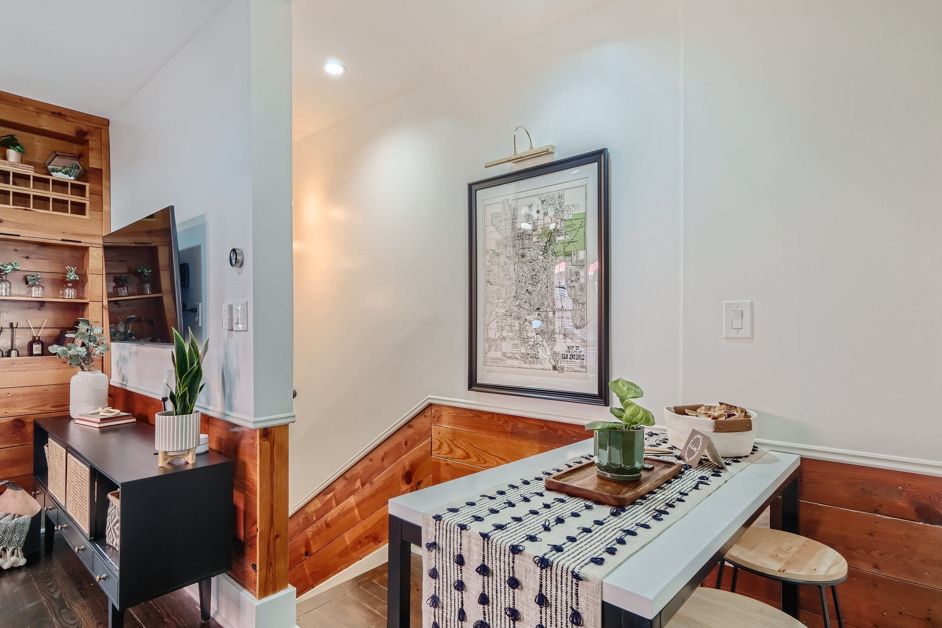 A modern kitchen with wooden cabinetry, a dining area with a long table, and a framed map on the wall.
