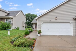 A residential driveway leading to a garage with a white door, surrounded by a well-maintained lawn and garden beds. - Spacious Kansas City Townhome with 2 Living Rooms Near Downtown Stadiums and MCI (Kansas City)