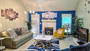 Een woonkamer met een open haard, een bank, een gele fauteuil en een salontafel.