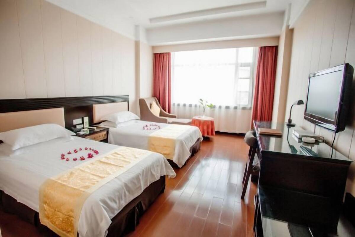 Habitación de hotel con dos camas, un escritorio, una silla, un televisor y una ventana con cortinas.