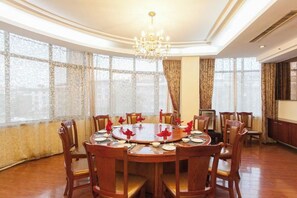 A dining room with a round table set for six, surrounded by wooden chairs, large windows with curtains, and a chandelier. - Dabieshan Hotel (Luotian County)