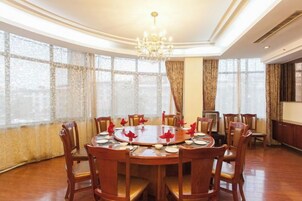 Comedor con una mesa redonda preparada para seis personas, rodeada de sillas de madera, ventanas amplias con cortinas y una araña.