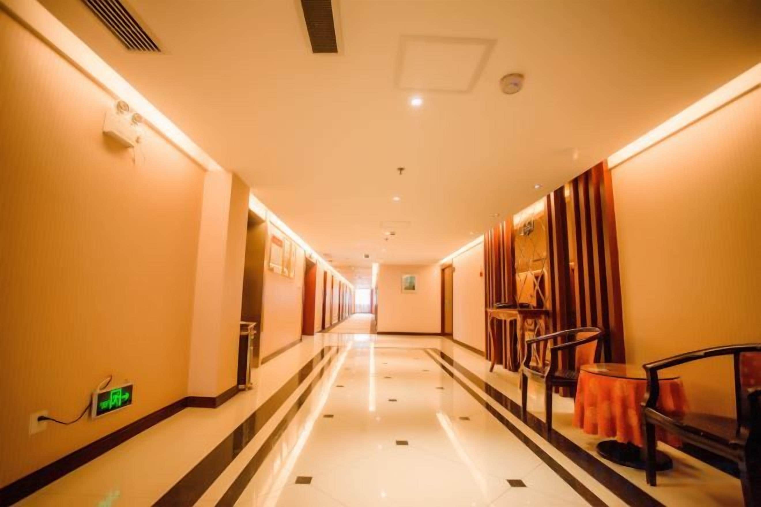A hotel corridor with a polished floor, doors on both sides, and a seating area with chairs and a table.