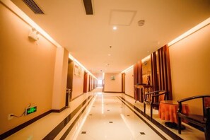 A hotel corridor with a polished floor, doors on both sides, and a seating area with chairs and a table. - Dabieshan Hotel (Luotian County)