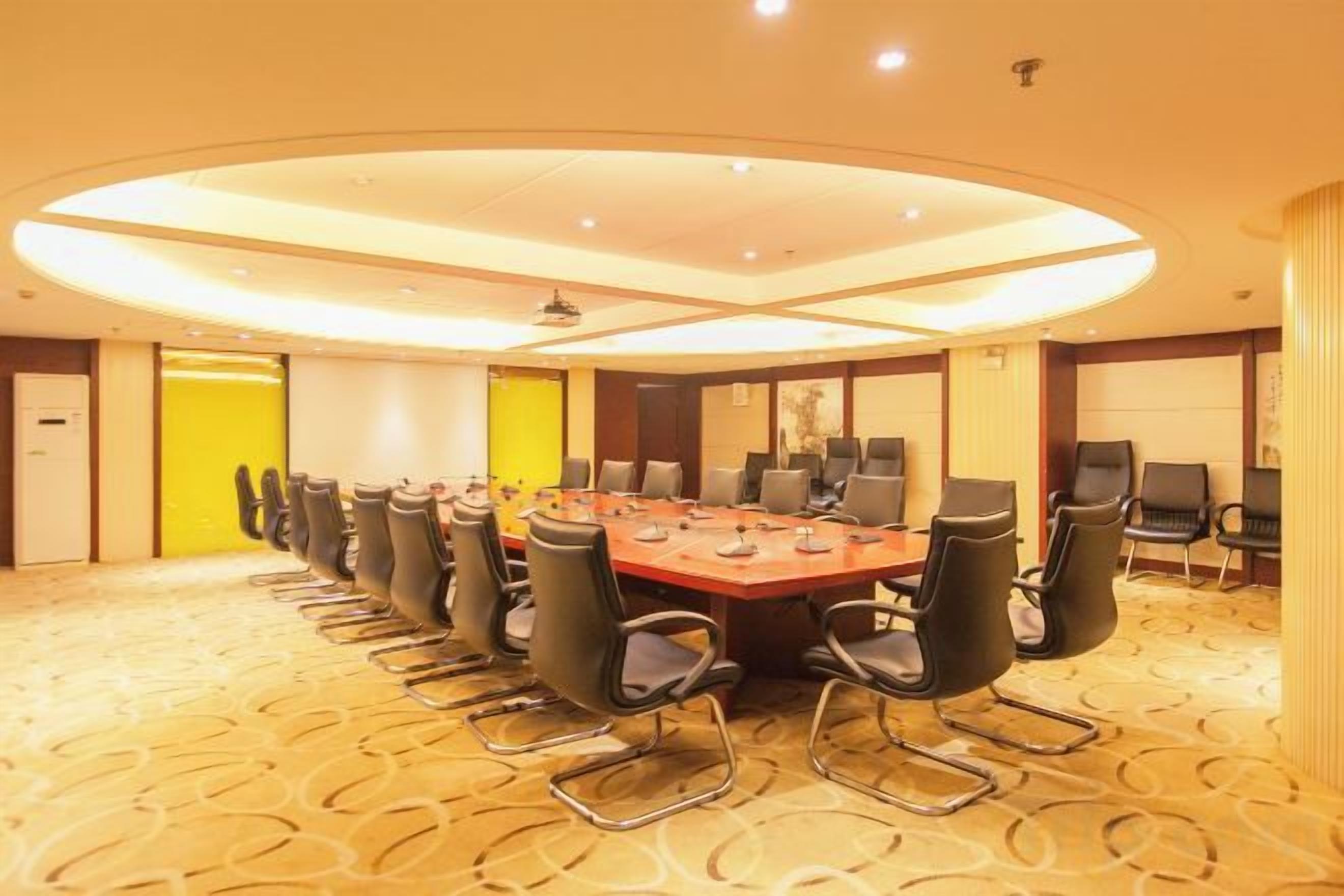 A conference room with a long table and multiple chairs, a projector screen, and a carpeted floor.