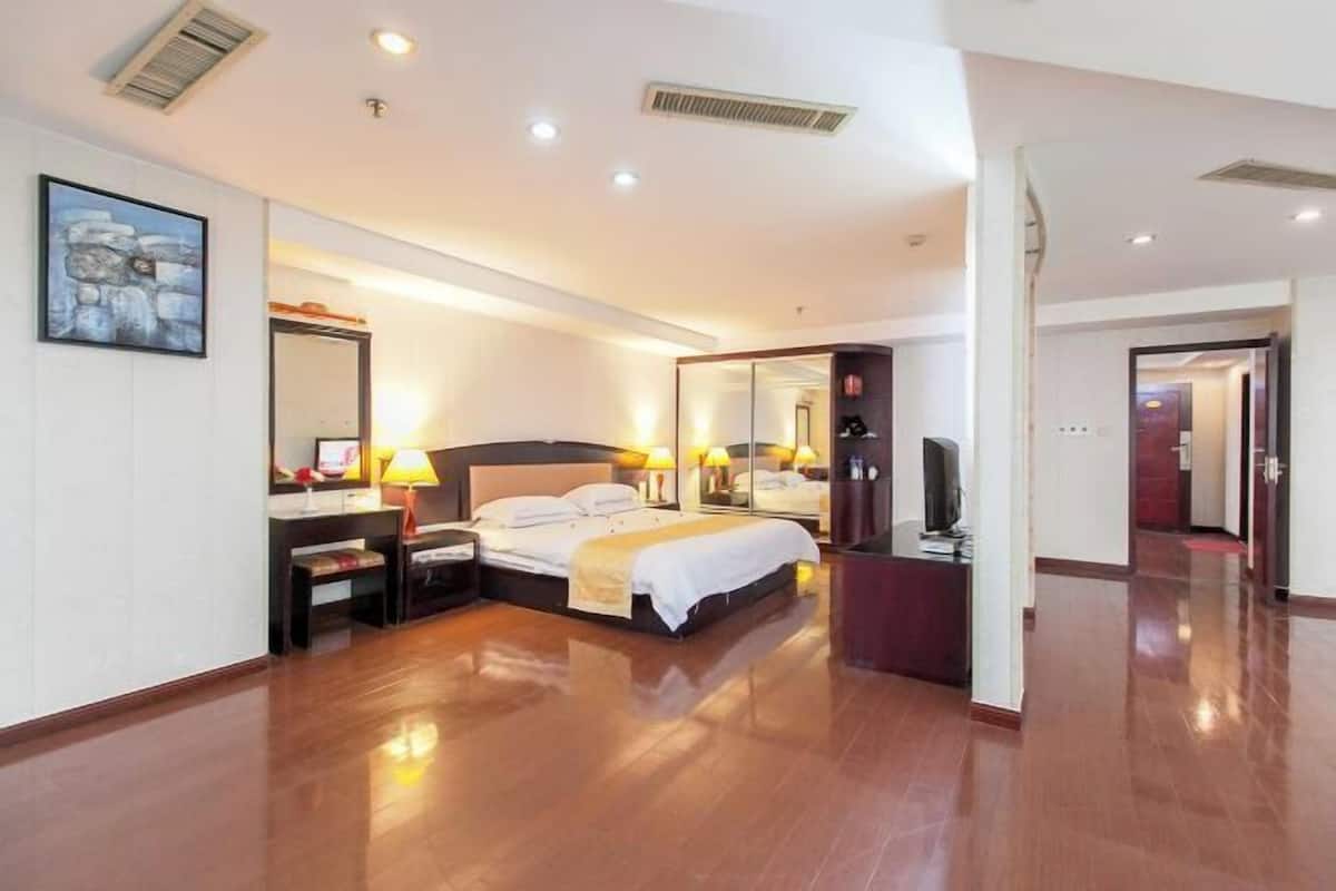 Una habitación de hotel con una cama, mesitas de noche, un escritorio, un espejo y un televisor.