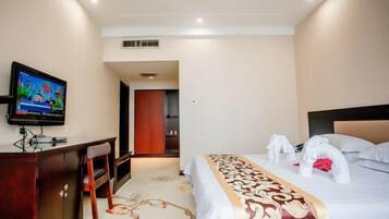 A hotel room with a bed, a desk, a television, and a door leading to another room.
