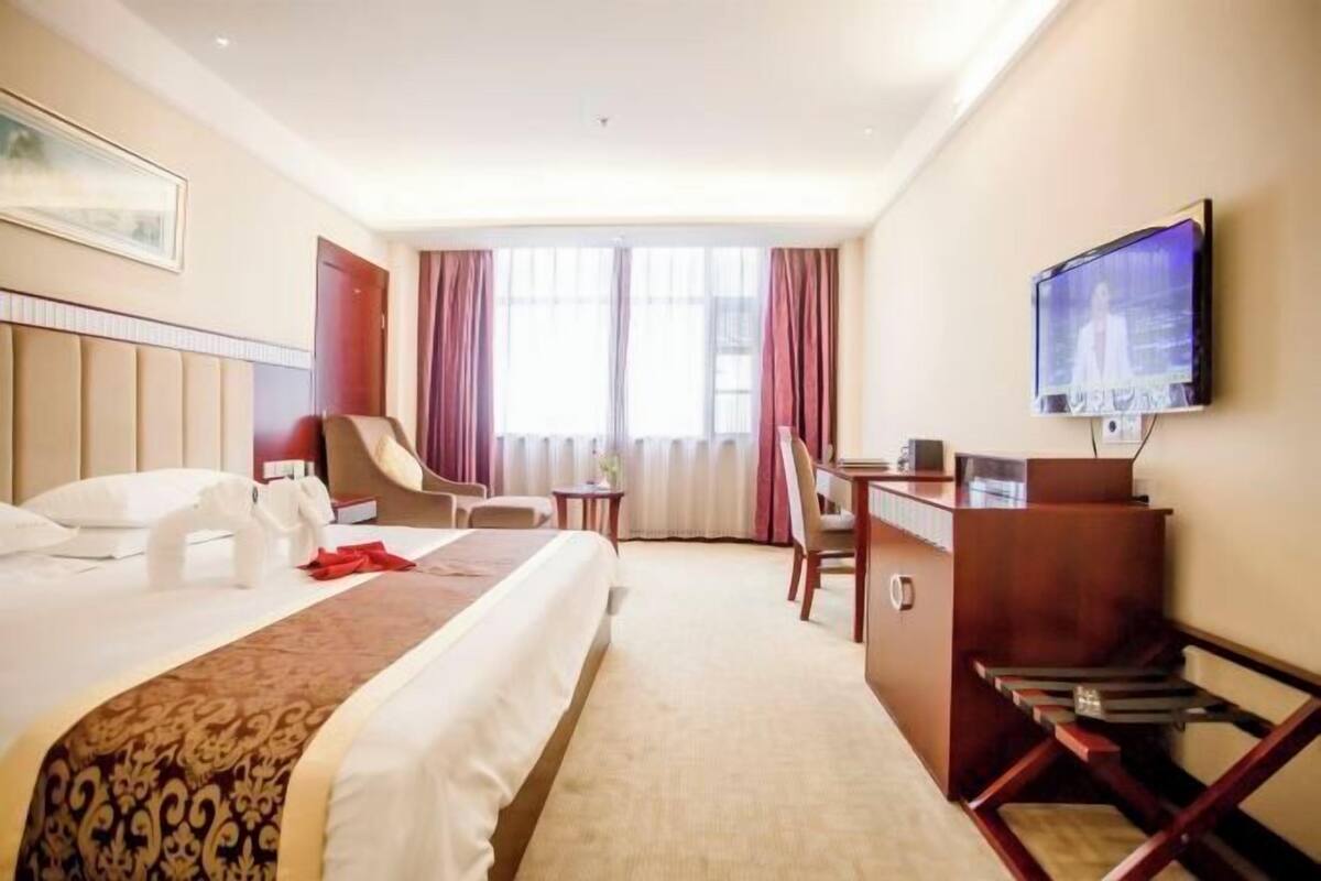 Habitación de hotel con cama, escritorio, silla, televisor y ventana con cortinas.