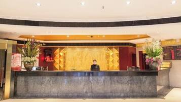 A hotel reception area with a marble counter, a receptionist, and decorative plants.