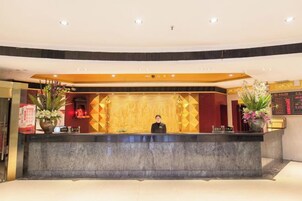 Zona de recepción de hotel con mostrador de mármol, una recepcionista y plantas decorativas.