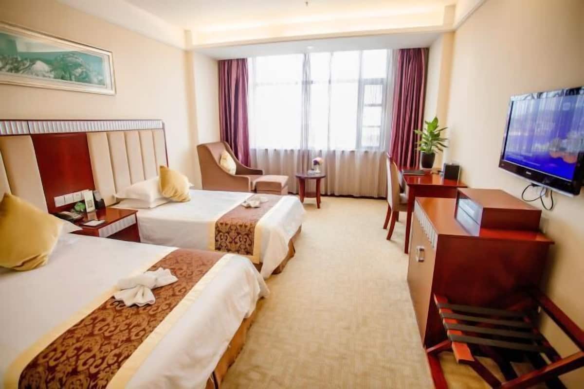 Habitación de hotel con dos camas, un escritorio con computadora, televisión y ventana con cortinas.