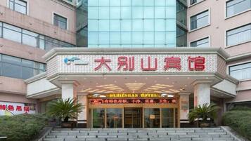 A hotel entrance with a sign in Chinese characters, a staircase leading up to the entrance, and two potted plants on either side.
