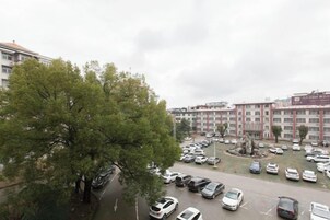Un estacionamiento con varios coches, un árbol grande y un edificio de varios pisos al fondo.