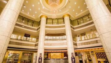 A multi-level hotel lobby with a grand chandelier, marble columns, and a reception desk.
