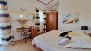 Un dormitorio con cama, escritorio, silla, armario, espejo y un cuadro en la pared.