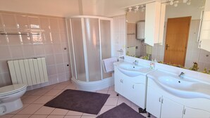 Un baño con ducha, dos lavamanos, inodoro y radiador.