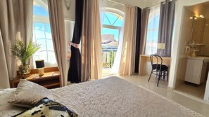 Un dormitorio con una cama grande, un escritorio, una silla y vistas al exterior.