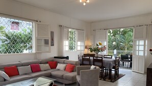 A modern living room with a sectional sofa, a glass coffee table, and a dining area with a table and chairs. - Magnificent villa with free parking ideally located. (Schoelcher)