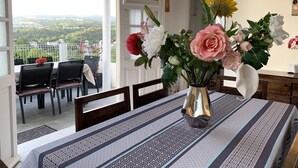 A dining area with a table set for two, a vase with flowers, and a view of a balcony with chairs and a railing. - Magnificent villa with free parking ideally located. (Schoelcher)
