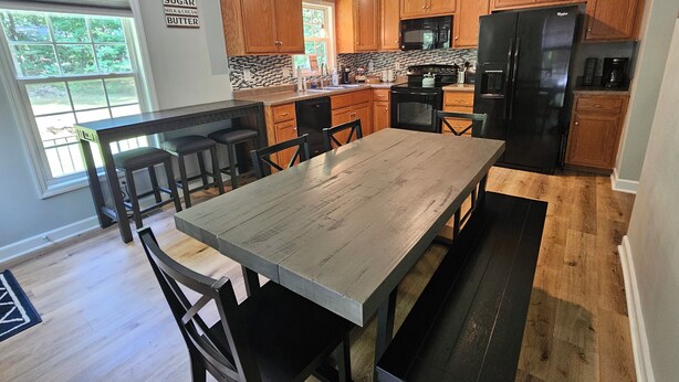 Een moderne keuken met houten kastjes, een zwarte koelkast en een eettafel met stoelen.