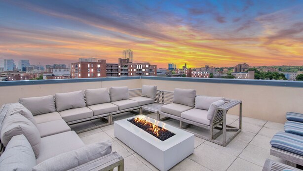 Une terrasse sur le toit avec un foyer, des sièges d’extérieur et une vue imprenable sur les toits de la ville au coucher du soleil.