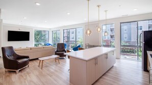 Un salon moderne comprenant un canapé, un fauteuil en cuir marron, une table basse et un îlot de cuisine avec des placards.