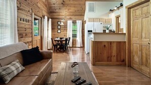 A wooden cabin interior with a living room, dining area, and kitchen.