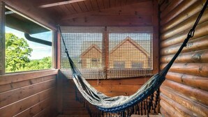 A hammock in a wooden cabin with a view of houses through a window.