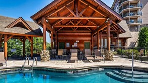 A wooden poolside area with lounge chairs and a covered seating area.
