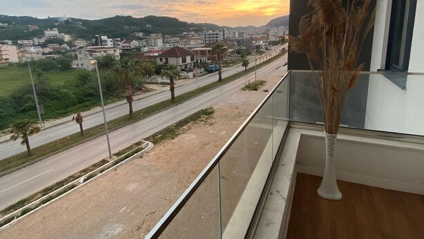 Een balkon met uitzicht op een stadsgezicht tijdens zonsondergang, een vaas met gedroogde planten en een heldere lucht.